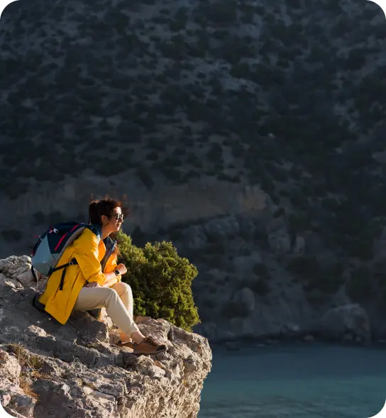 A hiker sitting on a rock looking out at the ocean