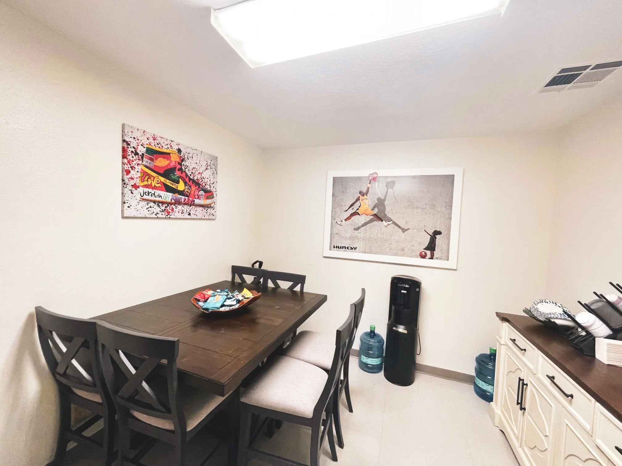 Mental Health Outpatient dining room. There is a dining room table and 3 chairs and a water dispenser. There is artwork hanging on the wall.