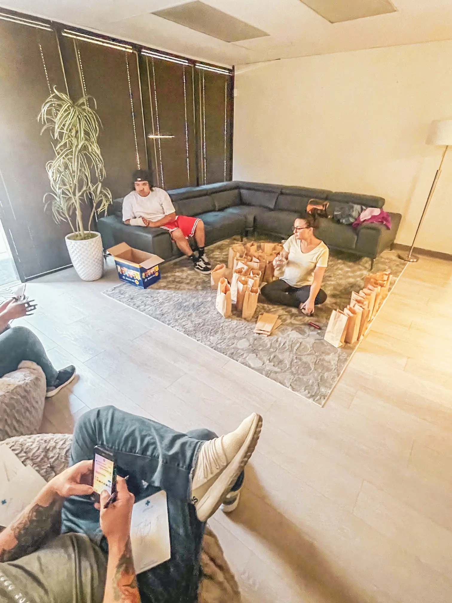 Mental health outpatient patients volunteer work. There are many paper bags with sandwiches in them sitting on the floor while a volunteer counts them.