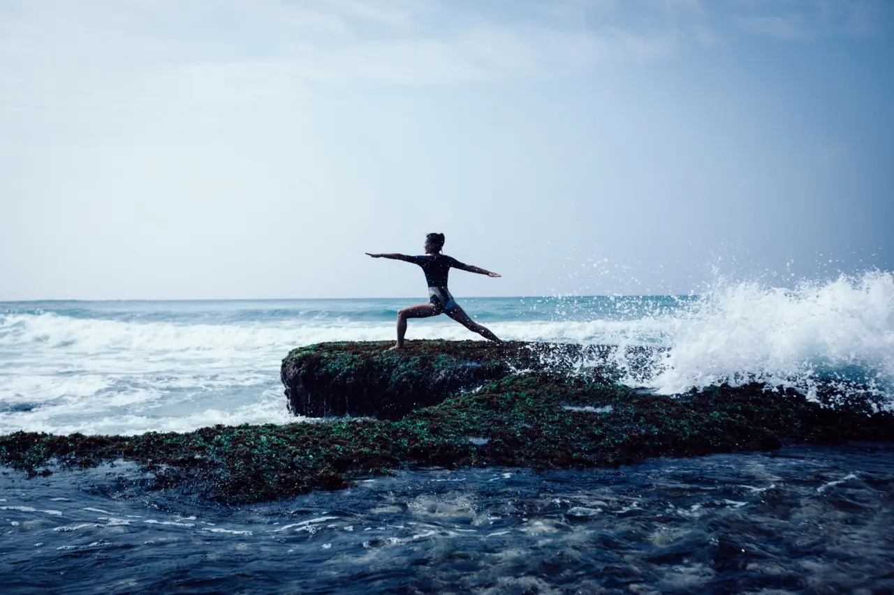 A person doing yoga on a rock in the ocean