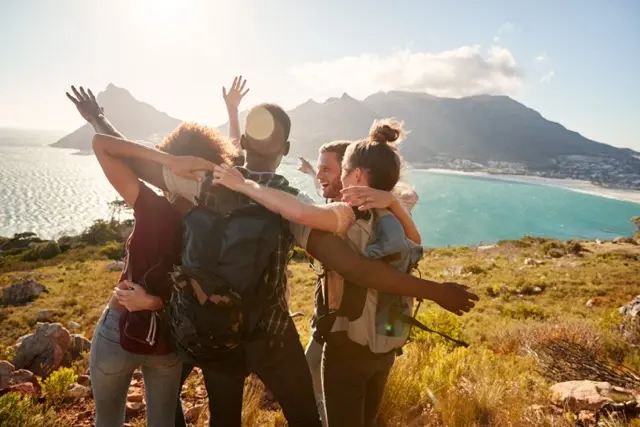 A group of friends hiking next to the ocean celebrating and hugging