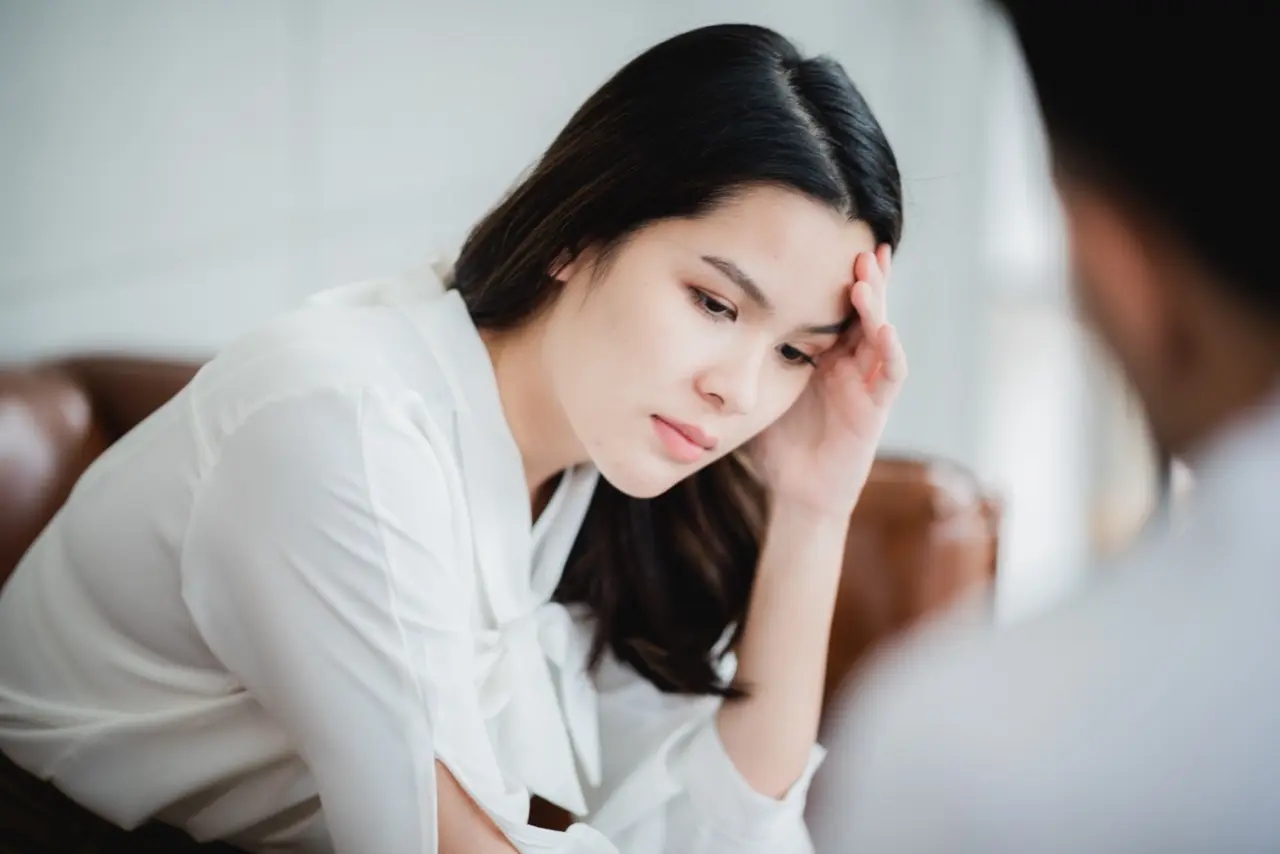 A young woman with depression sits on a couch with a hand on her forehead during a therapy session