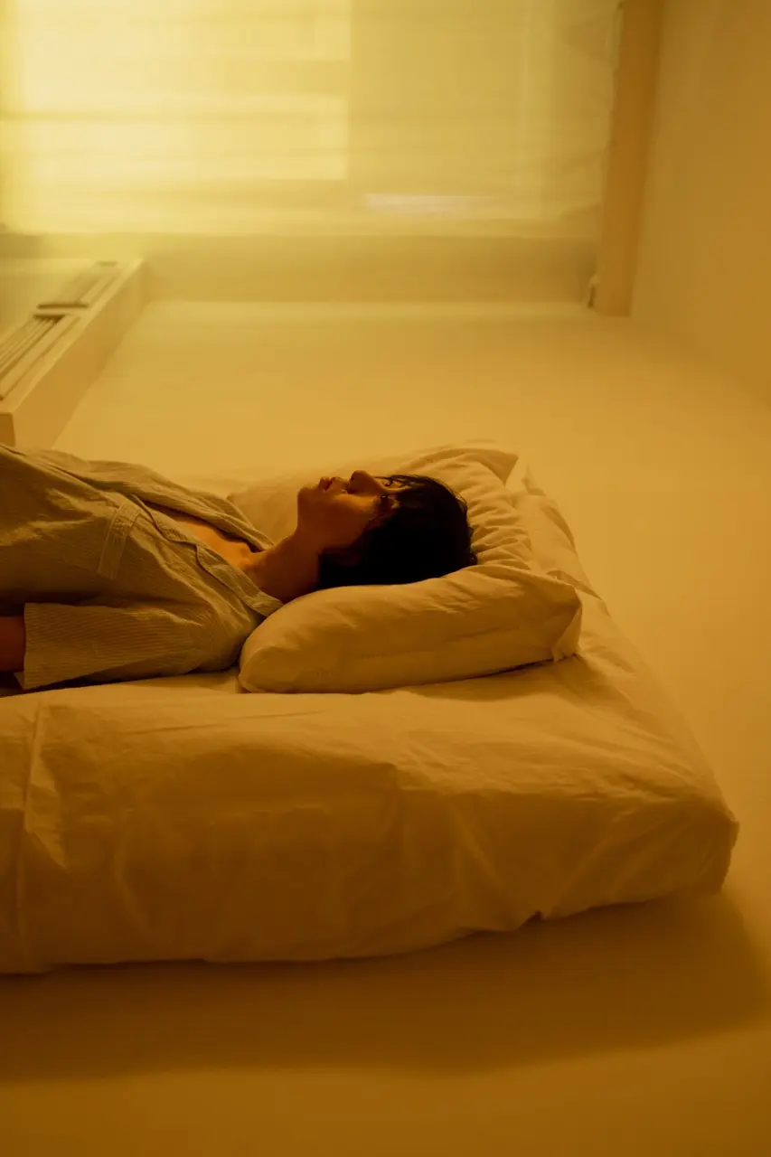 A woman lays on her mattress on the floor while staring at the ceiling