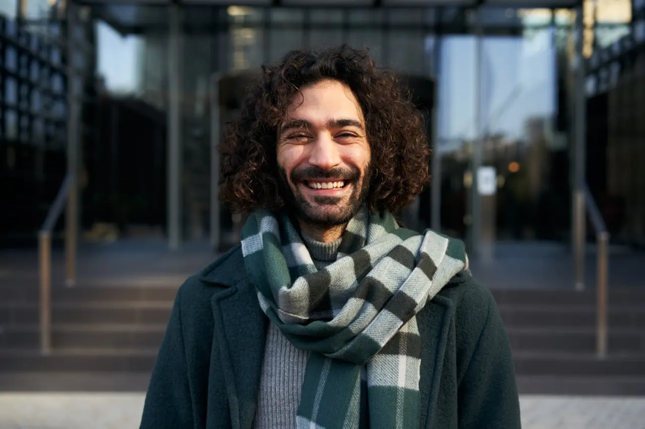 A young man with curly hair looking at the camera and smiling