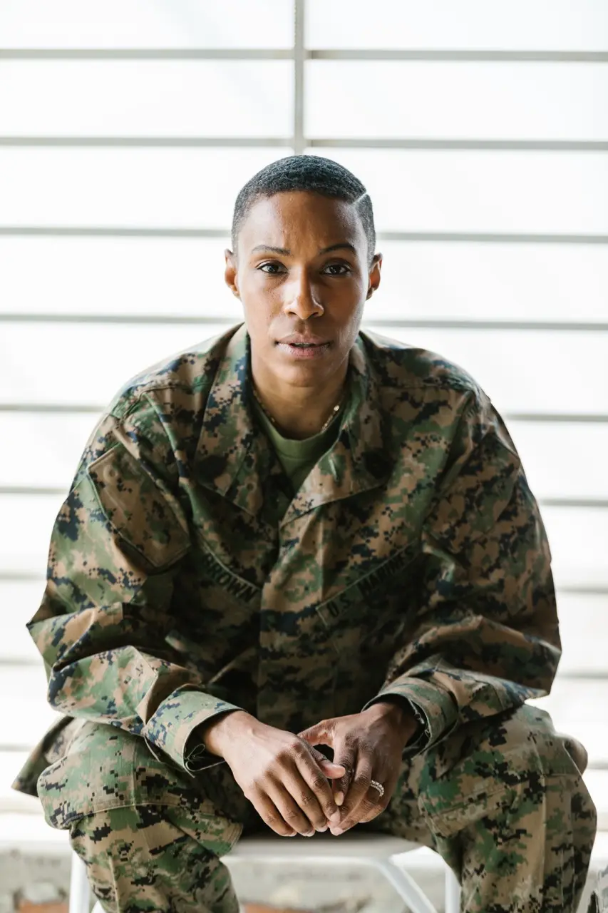 An African American woman with a buzzcut in a military uniform suffers from PTSD as she sits in a group therapy session for PTSD treatment