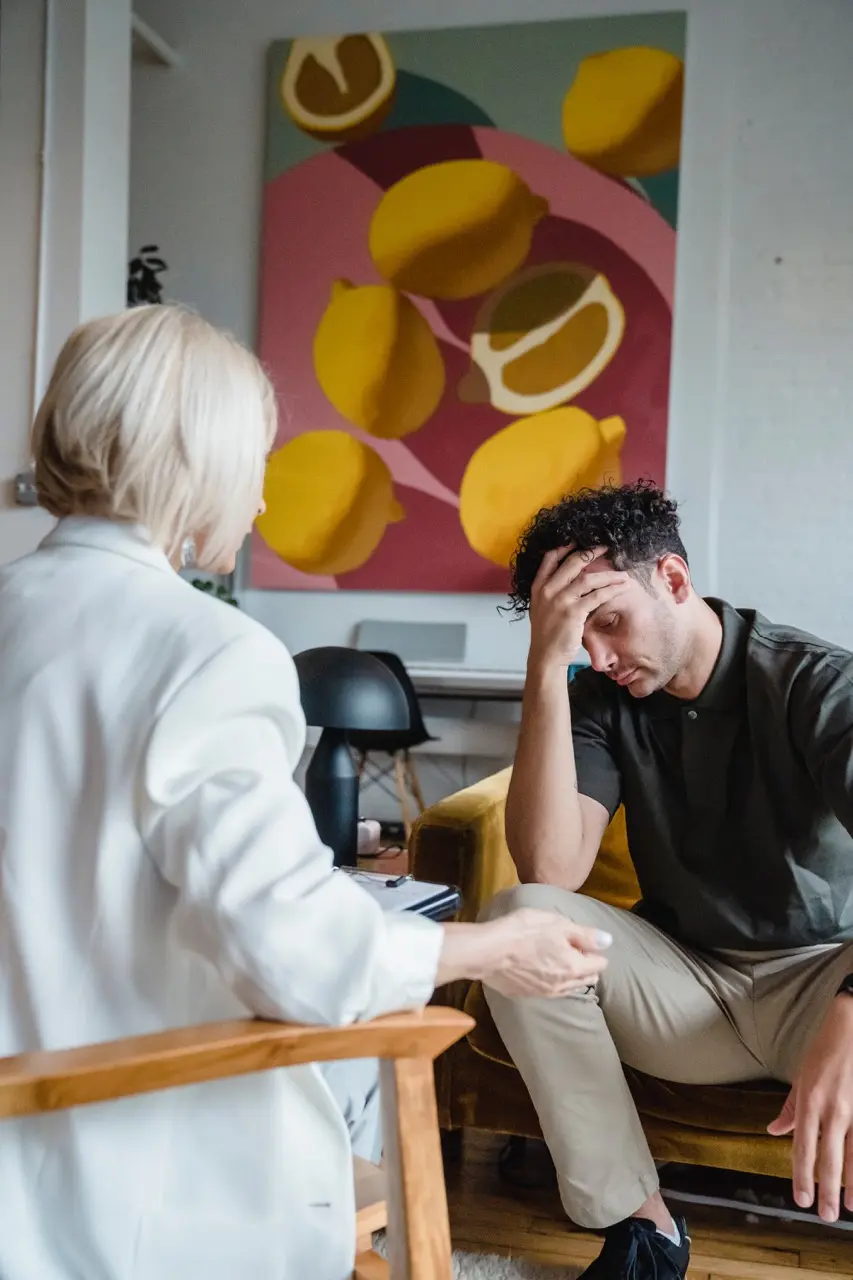 drug and alcohol abuse therapy session; a young man sits in his chair with his hand on his forehead while he's talking to his counselor who sits across from him