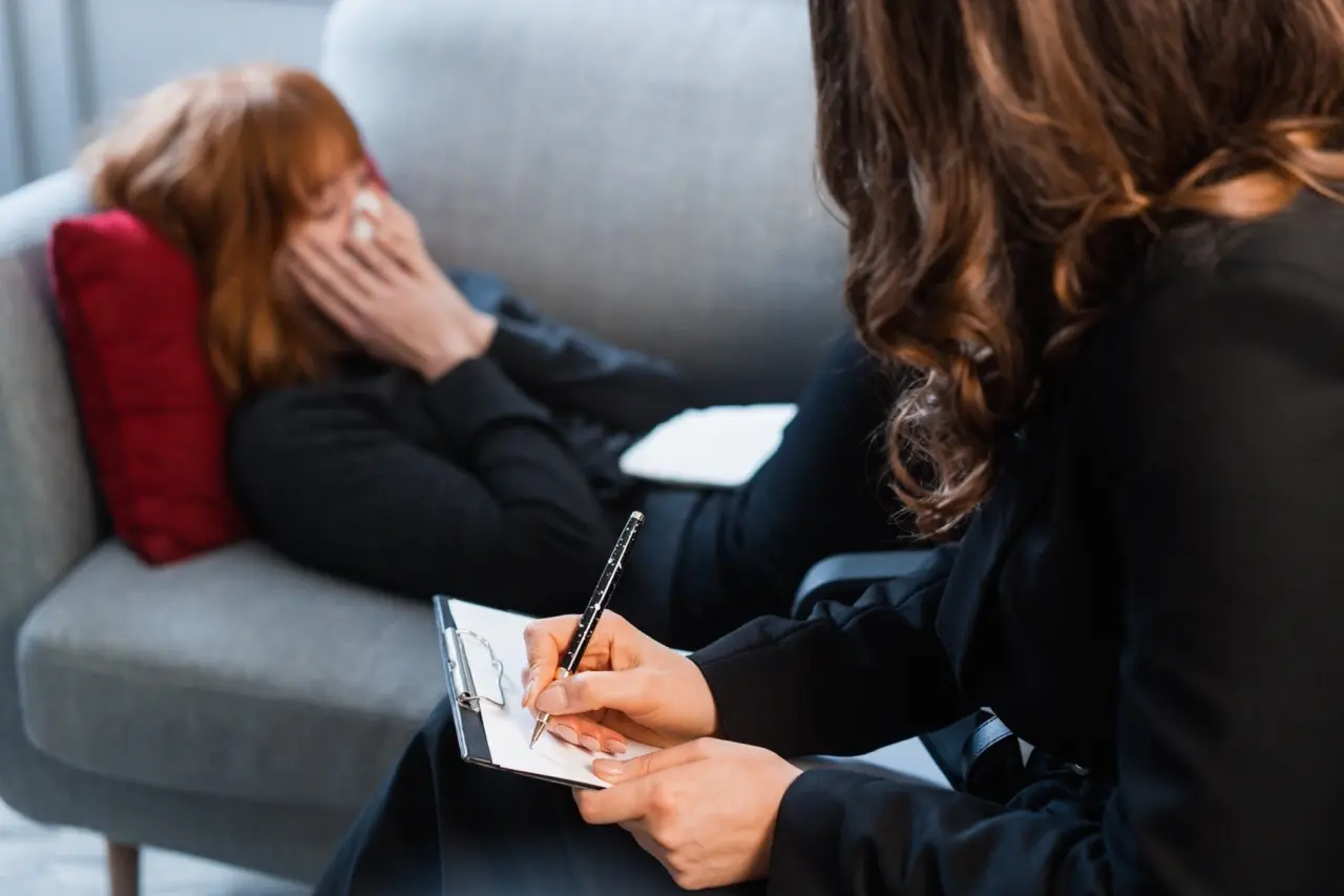 Orange County Anxiety Treatment Center at California Care: therapy session for anxiety; woman laying on the couch crying and holding a tissue to her face while her therapist sits across from her taking notes