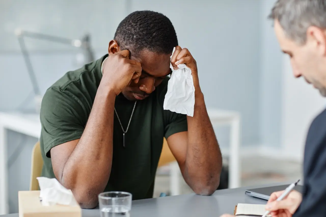 man sitting with hands on his face and holding a tissue while being counseled by therapist for a personality disorder